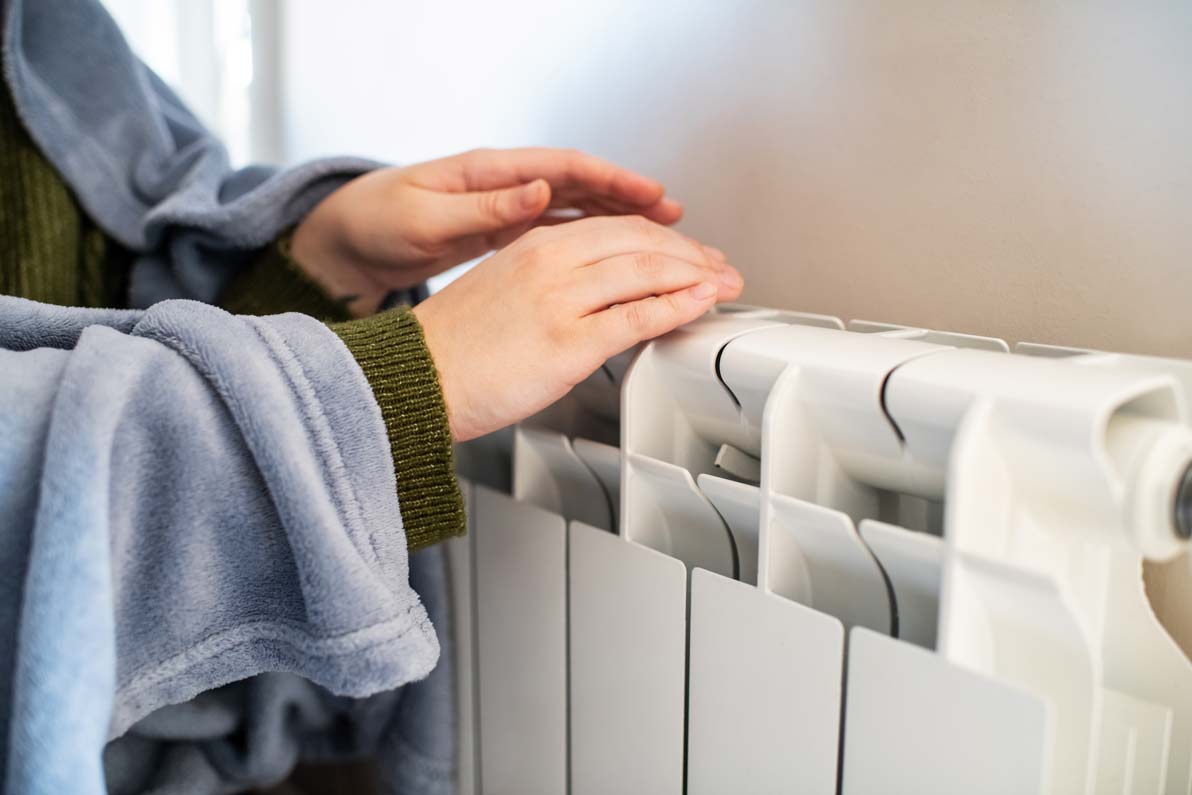 Woman trying to warm near a radiator in winter
