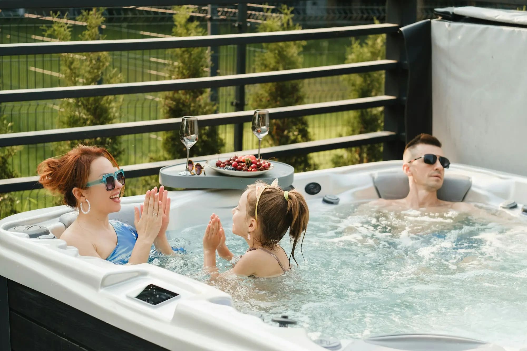 A family relaxes in a hot tub in their backyard surrounded by greenery in Grimes, IA.