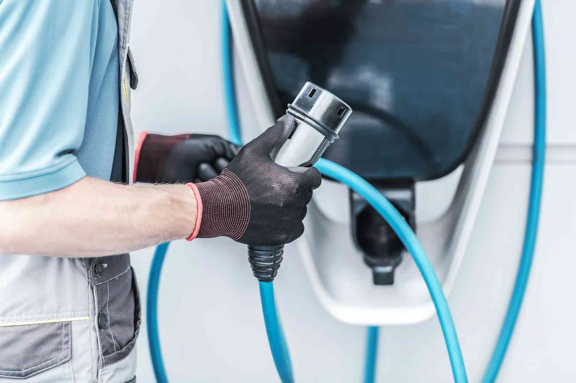 A man connects a hose to an electric vehicle during an EV charger installation in Grimes, IA.