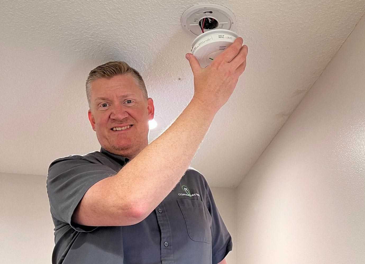 A man installs a smoke and carbon monoxide detector on a ceiling in Grimes, IA.