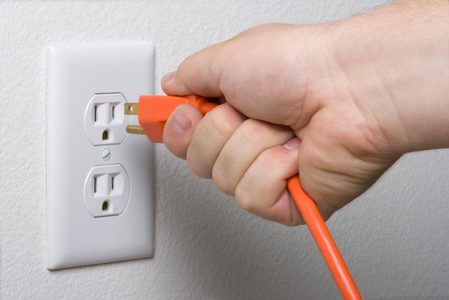 A person holds an orange surge protector cord, connecting it to a wall outlet in Grimes, IA.